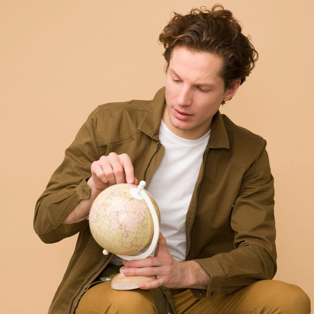 a sitting young man pointing at a globe curiously 